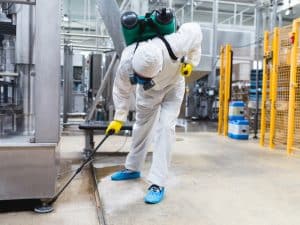 A professional pest controller in protective gear inspecting for signs of rodent infestation in an industrial facility.